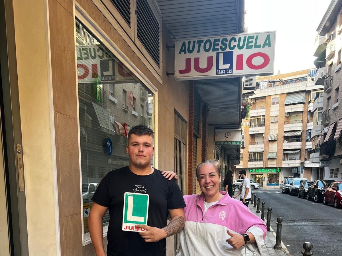 Alumno con la placa L junto a su profesora frente a Autoescuela Julio